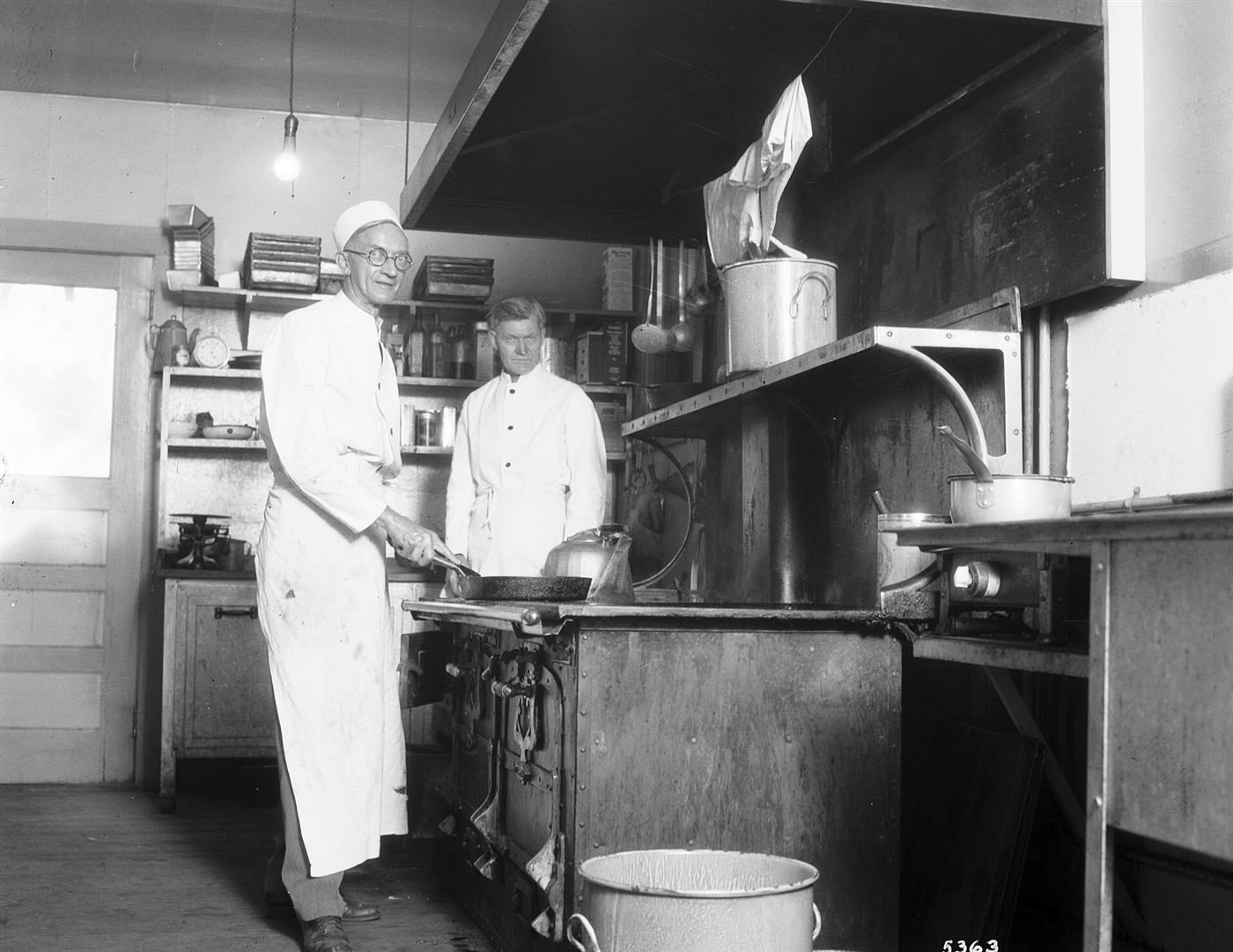 Dos cocineros con delantal junto a una cocina de hierro